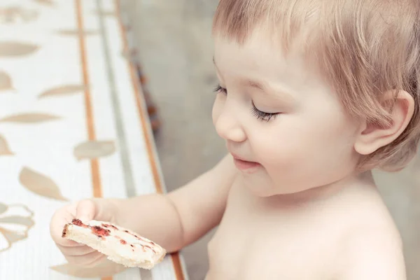 Голодна дитина сидить за кухонним столом і тримає бутерброд з джемом в руці . — стокове фото