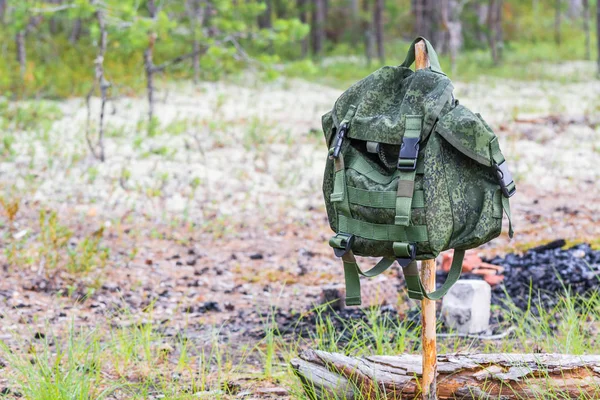 Un sac à dos vert pour la randonnée est accroché à la sangle sur fond de place pour le feu dans la forêt de conifères d'été . — Photo