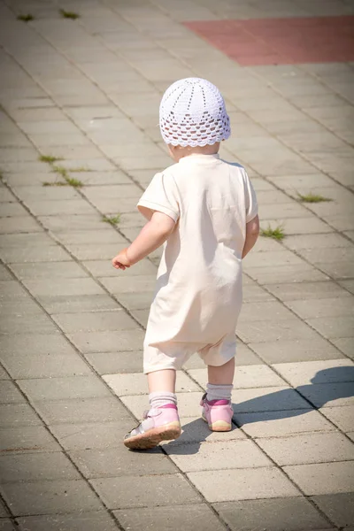 Маленька дитина в білому костюмі біжить по асфальтованій доріжці від набережної річкового порту — стокове фото