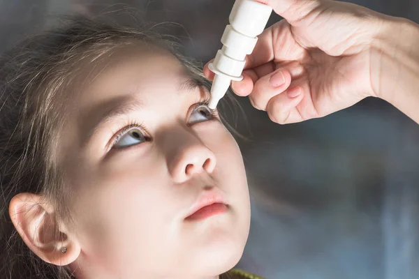 Mom eye drops dripping from the pain in the eyes of a beautiful child