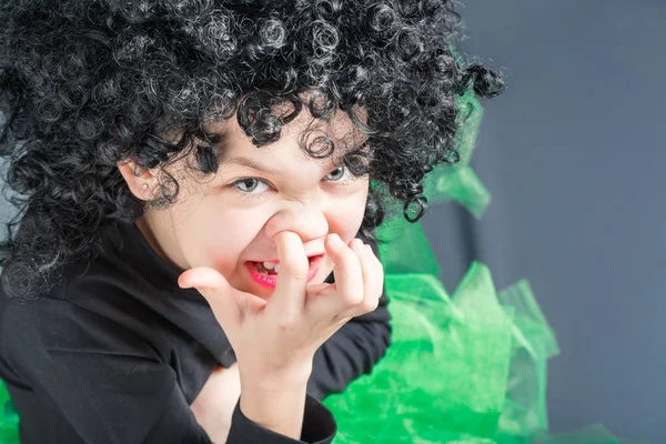 Beautiful girl in a black curly wig and a dancing suit picks her finger in the nose