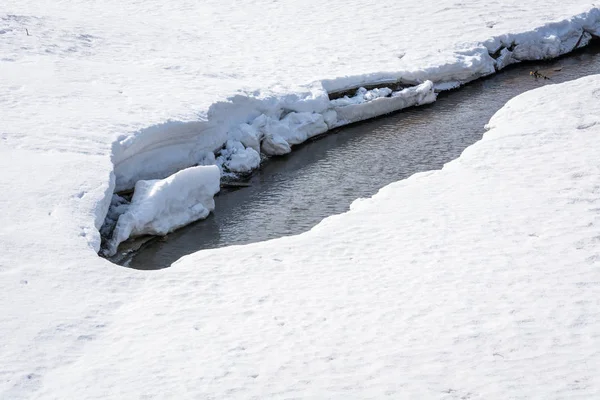 Довга тха тече під білим снігом навесні на річці . — стокове фото