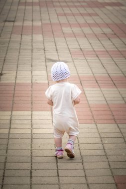 Nehir limanının rıhtımından asfalt yolun etrafında koşan beyaz takım elbiseli küçük bir çocuk.