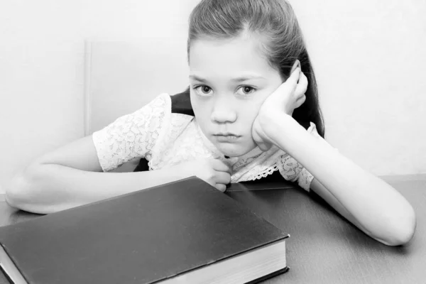 Menina triste bonita senta-se a uma mesa com um livro — Fotografia de Stock