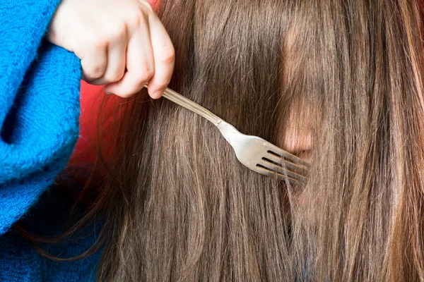 Schattig meisje in een blauwe trui is borstelen haar haar met een vork over een rode achtergrond — Stockfoto