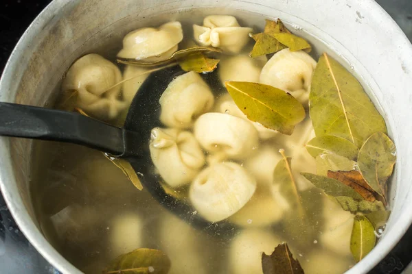 Ordinary handmade meat dumplings with bay leaves on ladle above the saucepan. — Stock Photo, Image