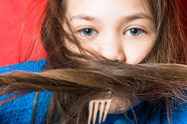Cute little girl in a blue sweatshirt with a fork in her mouth on a red background