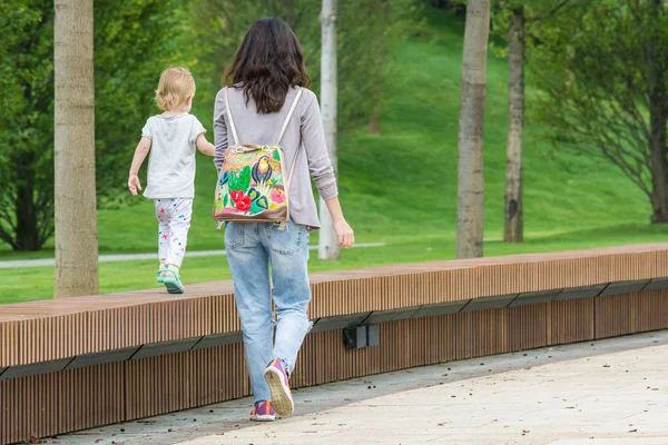 クラスノダール、ロシア - 6月 7, 2018: 美しいバックパックを持つ若い母親は、手で小さな子供と一緒に歩きます. — ストック写真