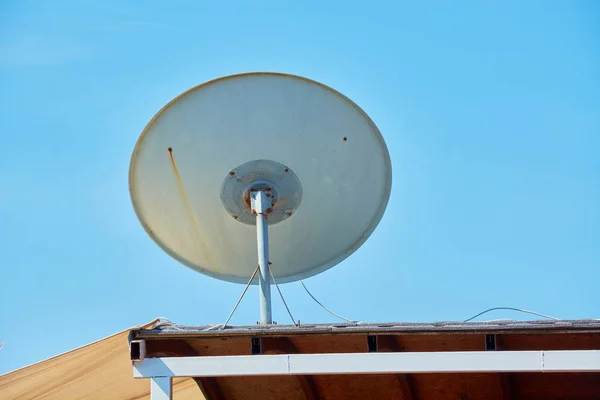 Duża okrągła antena zamontowana na dachu budynku rozmieszczonego na błękitnym niebie. — Zdjęcie stockowe