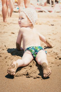 Beyaz sunhat güzel bebek plaj ve güneşlenmesıcak kum yatıyor.