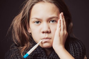 Siyah eşarplı hasta kız, başında bir el ile ağızda termometre tutan sıcaklığı ölçer.