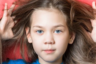 Mavi bluz sevimli kız kırmızı bir arka plan üzerinde parmakları ile saçlarını taramaya çalışır