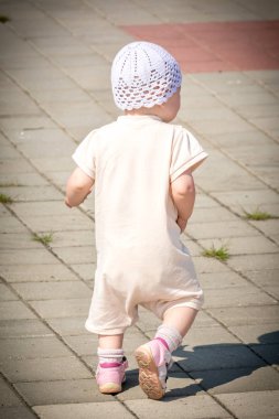 Nehir limanının rıhtımından asfalt yolun etrafında koşan beyaz takım elbiseli küçük bir çocuk.