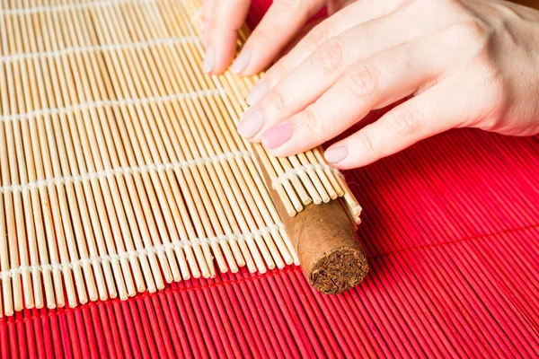 Female hands tightening fresh cigar with the help of bamboo mat, concept of making cigars.