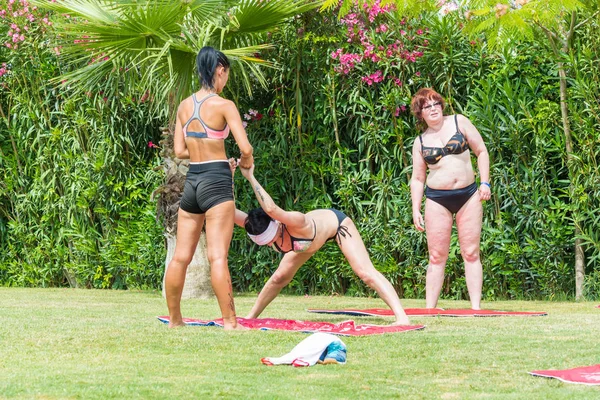 Side, Turquía - Junio 2018: Entrenador de yoga estira los músculos de una anciana sobre hierba verde . — Foto de Stock