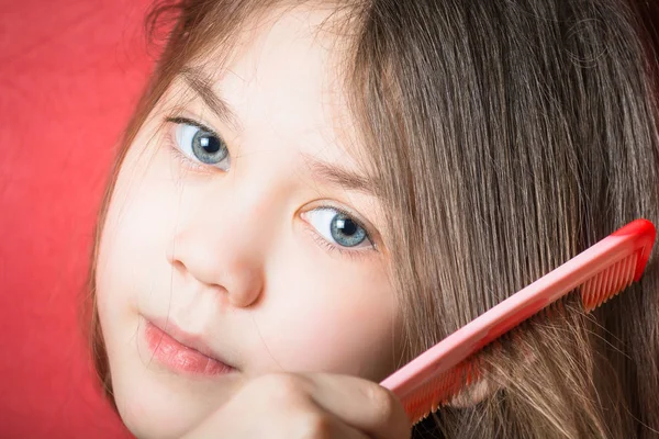 Beautiful girl combs her hair on a red background — Stock Photo, Image