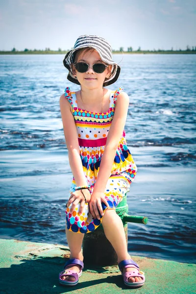 Красива дівчина в капелюсі і окулярах сидить на пірсі на річці — стокове фото