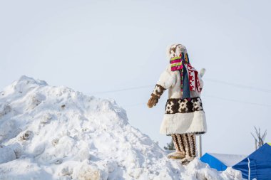 Russkinskaya, Rusya - 24 Mart 2018: Kuzeydeki geyik derisi ve kürkten yapılmış ulusal kuzey kıyafetleri giyen Hanty çocuk, merkez meydandaki karlı dağa tırmanıp uzaklara bakıyor. Tatil 
