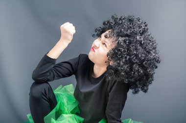 Siyah kıvırcık peruk ve dans kıyafeti güzel kız bir yumruk gösterir