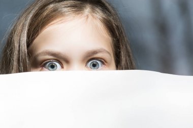 Large eyes of a frightened child peeking around a sheet of paper clipart