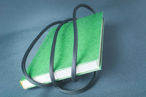 Livro verde é enrolado em fio preto — Fotografia de Stock