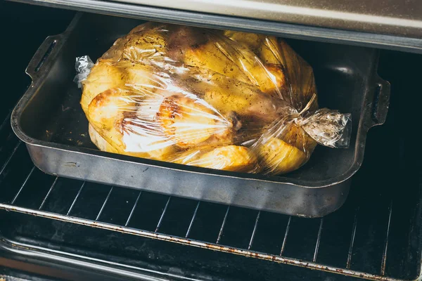 Hähnchenkeule und Kartoffelscheiben im Bratbeutel auf Backblech im Ofen. — Stockfoto