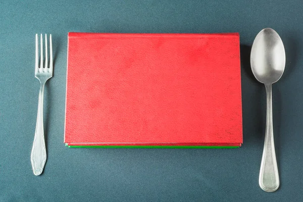 Cuchara de plata y tenedor se encuentran cerca de una pila de libros de colores — Foto de Stock