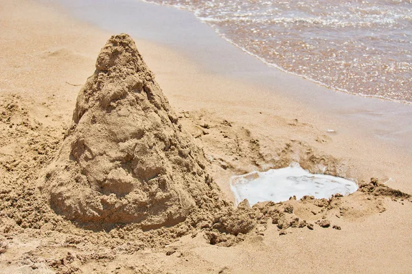 Montagne sablonneuse avec fosse creusée pour l'eau sur les rives de la plage de mer . — Photo