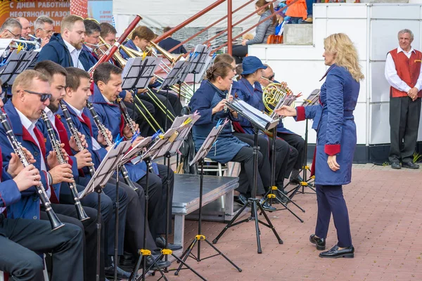 スルグト、ロシア - 2018年9月2日:女性指揮者がパイプとサックスを演奏する男女の交響楽団を指揮します。石油・ガス産業の休日労働者. — ストック写真