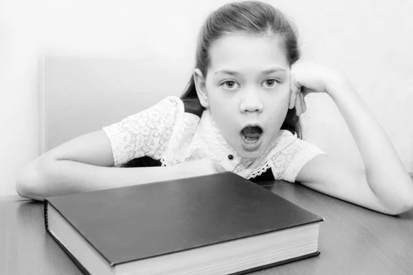 Belle fille triste bâillant assis à une table avec un livre — Photo