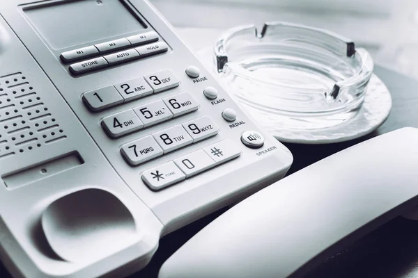 Telefone branco com o telefone apanhado perto do cinzeiro de vidro para fumar na mesa de madeira . — Fotografia de Stock