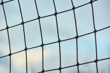 Bulutlarla mavi gökyüzüne karşı halattan yapılmış bağlı voleybol ağı.