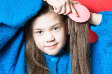 Mavi kazak sevimli kız kırmızı bir arka plan karşı saçlarını fırçalama olduğunu