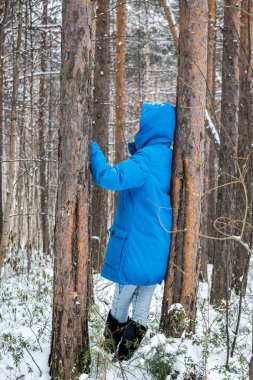 Kış ormanda kız dondurulmuş ağaçları kucaklıyor.