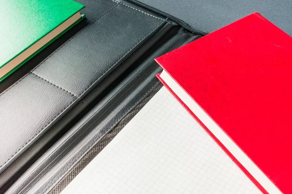 Gröna och röda böcker ligger i en öppen svart lädermapp med en anteckningsbok — Stockfoto