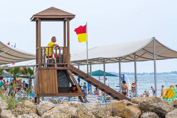 Lado, Turquía - Junio 2018: El salvavidas se sienta en una torre de madera y observa cómo se bañan en el mar . —  Fotos de Stock