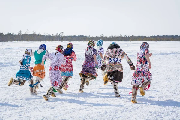 Russkinskaya, Rusia - 24 de marzo de 2018: Mujeres khanty en la ropa nacional del norte corren la cruz en dirección al bosque. Competición en la carrera entre las chicas. Fiesta de los pastores de renos d — Foto de Stock