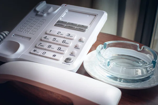 Telefone de escritório com o telefone apanhado perto do cinzeiro de vidro para fumar na mesa de madeira . — Fotografia de Stock