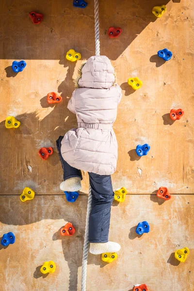Kış giysileri korkusuz kız oyun üzerinde yardım ipi ile duvara tırmanıyor.