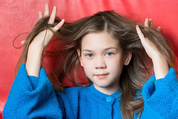 Jolie fille en chemisier bleu essaie de peigner ses cheveux avec les doigts sur un fond rouge — Photo