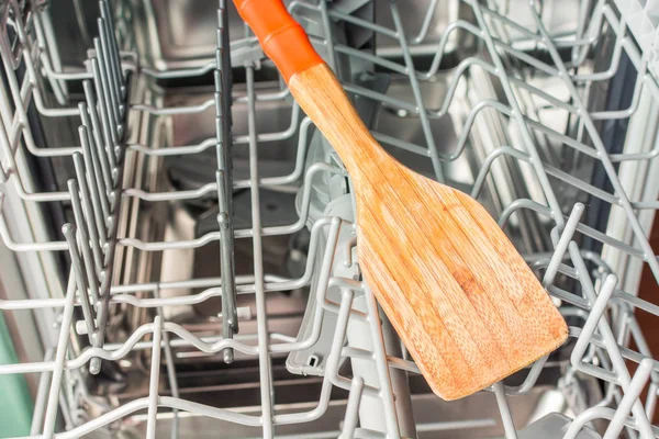 Желтая деревянная лопатка лежит в середине отсека посудомоечной машины — стоковое фото