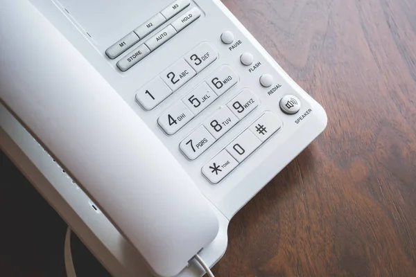 Büyük düğmeli beyaz telefon ve ahşap masa üzerinde tüp..