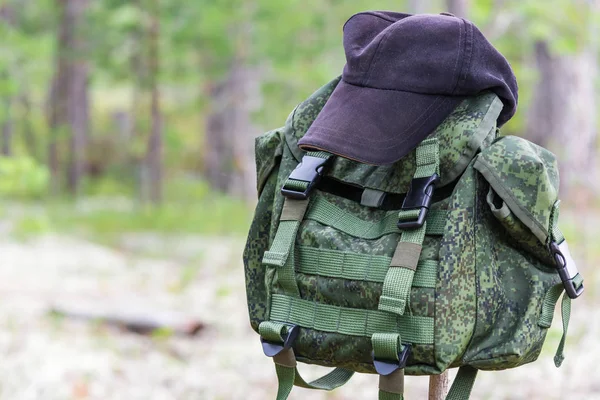 Sac à dos pour les activités de plein air accroché à un bâton de bois sur le dessus est casquette noire dans la forêt d'été . — Photo