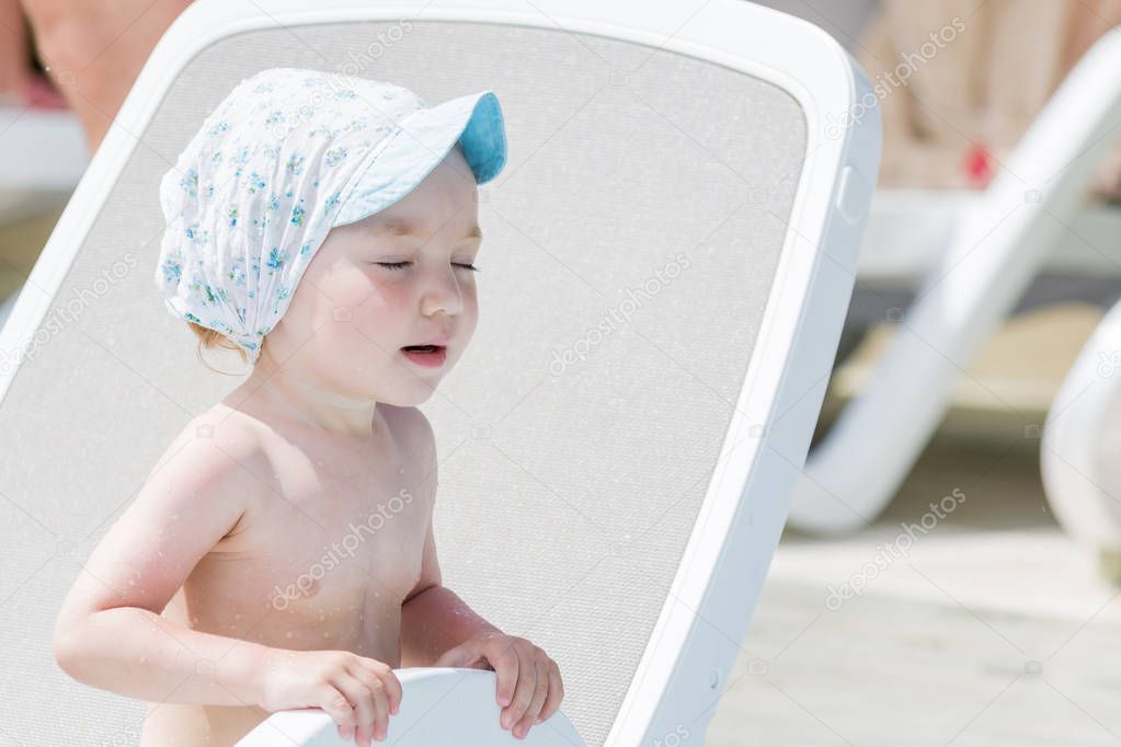 Frozen baby sunbathes on lounger with eyes closed and mouth open after swimming in the pool.