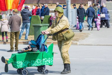 Surgut, Rusya - 9 Mayıs 2018: Askeri üniformalı, başında kasklı kadın, çocuk pusetinde uçak şeklinde yapılmış. Zafer Bayramı 9 Mayıs.