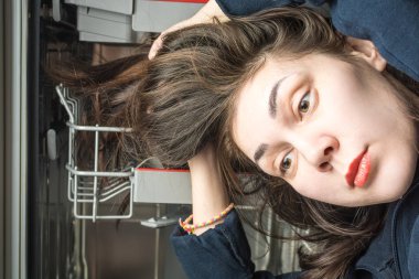 Girl lays long greasy hair in the dishwasher compartment clipart