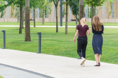 Krasnodar, Rusya - 7 Haziran 2018: İki genç kız yeşil çimboyunca cadde boyunca yürüyor.