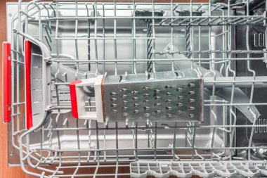 Iron grater with a red handle lies in the dishwasher clipart