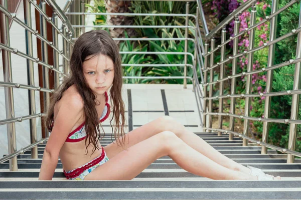 Chica ofendido en traje de baño con piernas largas sentado en una gran escalera . — Foto de Stock