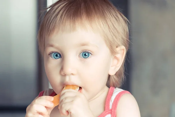 Удивлённый ребёнок с большими голубыми глазами, поедающий апельсиновый ломтик . — стоковое фото